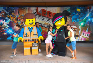 孩子們在主題公園裡微笑地站在巨大的LEGO Emmet和Wyldstyle雕像旁邊。