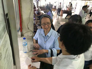 一位修女在繁忙的社區中心微笑著將紙張遞給訪客。