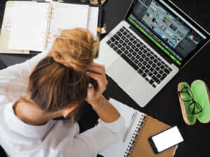 女性在雜亂的辦公桌上使用手提電腦、筆記本和電話，工作壓力大。