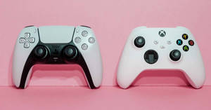 粉紅色表面上的兩個視頻遊戲控制器 PlayStation 和 Xbox