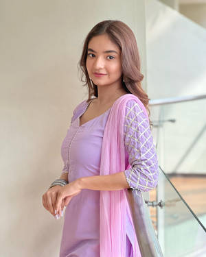 身穿薰衣草色傳統服飾的年輕女性在室內玻璃欄杆旁微笑。