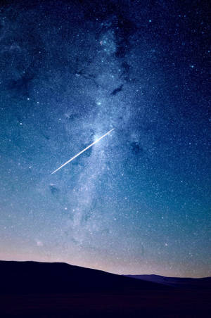 一顆明亮的流星在黑暗山丘上方的星空中留下一道軌跡。