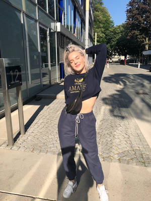 年輕女性穿著休閒街頭服飾，在現代建築附近的陽光人行道上擺姿勢。