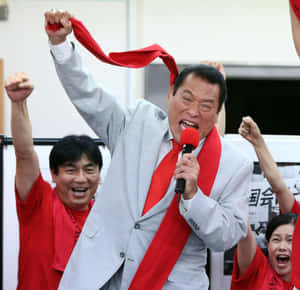 身穿灰色西裝、打紅色領帶的男子對著麥克風大喊，舉起拳頭和紅絲帶。