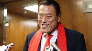 西裝紅色呔男士喺記者會微笑。