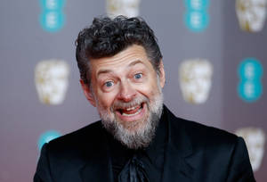 演員安迪·瑟克斯穿著黑色西裝在BAFTA活動中咧嘴大笑。