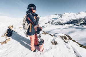 滑雪板運動員穿橙色褲子站在雪白山脊上俯瞰山谷