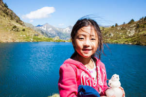 年輕女孩在陽光明媚的日子裡在山湖邊抱著雪人公仔