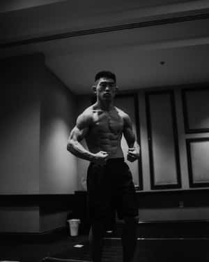 一個赤膊的肌肉發達男人站在健身房，表情專注。 — 成振宇 壁紙
