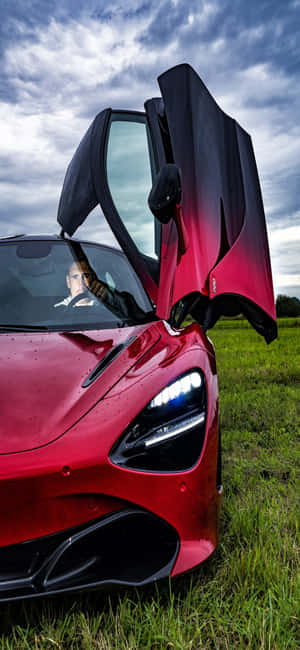 紅色McLaren跑車，鷗翼門打開，停在草地上。 — Galaxy A35 壁紙