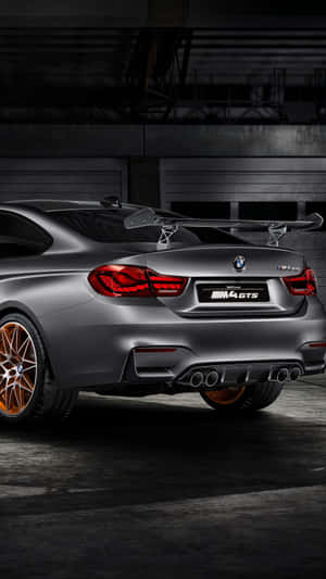 昏暗工業車庫中的啞光灰色BMW M4 GTS，配備銅色輪圈。