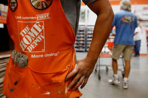 身穿橙色圍裙的 Home Depot 工人在商店通道中拿著工具。