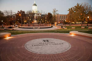 大學校園黃昏時分，圓形磚砌廣場上刻有「Mizzou Legacy Circle」。