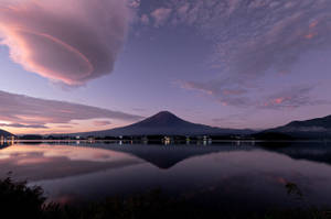 富士山在暮色中倒映在湖中，帶有粉紅色和紫色的雲彩。