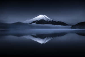 富士山在平靜的水面上倒映，天空陰暗有霧。