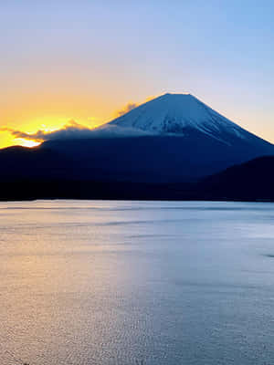 日落時分，白雪覆蓋的富士山頂倒映在平靜的水面上。 — iPad 壁紙