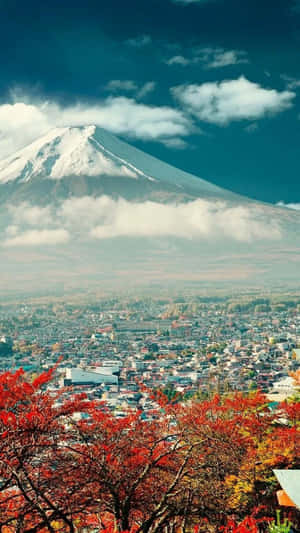 富士山頂覆蓋白雪，俯瞰著被秋葉紅樹環繞的城市。