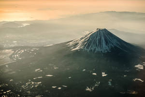 白雪覆蓋的富士山沐浴在金色的日出光芒中，下方是霧氣繚繞的山谷。