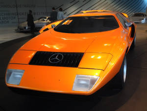 橙色 Mercedes-Benz 跑車在博物館展出，背景有人群。 — 汽車 壁紙