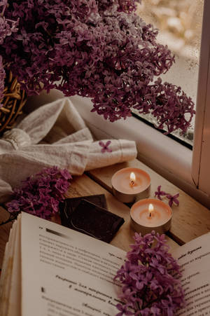 木窗台上的紫色丁香蠟燭和打開的書，柔和光線。