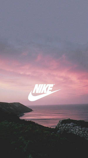 Nike標誌疊加在粉紅色和紫色的日落上，海洋上方有岩石峭壁。 — 沙灘 壁紙