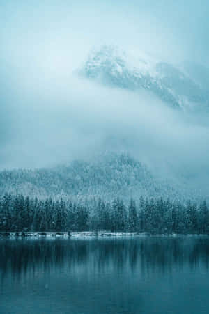 積雪的山巒和森林倒映在霧氣籠罩的天空下平靜的冬日湖面上。 — POCO Pad 壁紙
