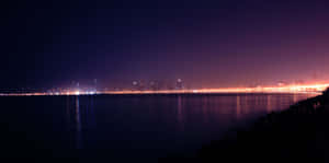 夜晚城市燈光倒映在平靜的水面上，天空呈現紫色。 — 天際線 壁紙