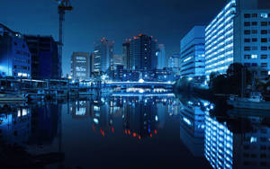 夜間城市天際線倒映在平靜的水面上，有發光的建築物和一座橋樑。 — 夜景城市 壁紙