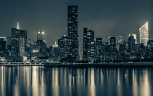 夜間城市天際線，燈火通明的摩天大樓倒映在平靜的水面上。 — 紐約市 壁紙