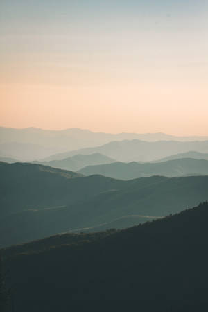 黃昏時分的寧靜山脈，層層山丘在粉彩天空下逐漸消失在霧中。