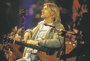 Kurt Cobain 在演唱會期間在舞台上彈奏木結他，身後有觀眾。
