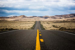 一條空蕩蕩的道路，帶有黃色中心線，穿過乾燥的景觀通往遠方的丘陵。