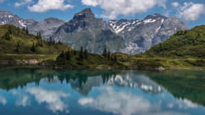 高山湖泊映照著積雪的山脈和雲朵，在清澈的藍天下。 — 美景 壁紙