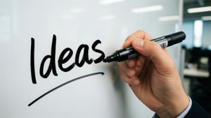 用黑色馬克筆在白板上寫下 Ideas 這個詞的手。