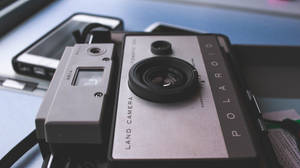 復古Polaroid相機放在藍色桌子上的智能手機旁邊。