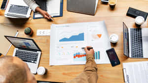 Two people reviewing business analytics charts on a wooden desk with laptops and coffee.