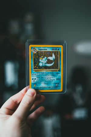 手拿著一張裝在透明保護套中的 Vaporeon 寶可夢交換卡。