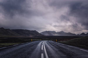 一條空路在陰天中蜿蜒穿過陰鬱的山景。 — 天氣 壁紙