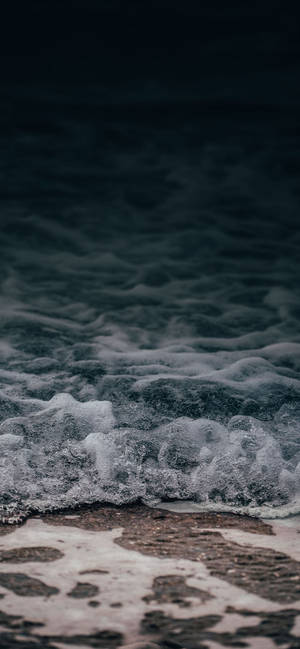 泡沫海浪沖刷黑暗沙灘的暮色景象 — iPhone 17 Pro 壁紙