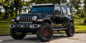 黑色Jeep Wrangler配紅色輪圈在陽光下停泊在戶外。