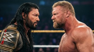 兩名職業摔角手在摔角擂台上對峙，背景有觀眾。 — Roman Reigns 壁紙