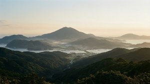 日出籠罩著薄霧的沿海山脈和海灣，有綠色山丘和小鎮。