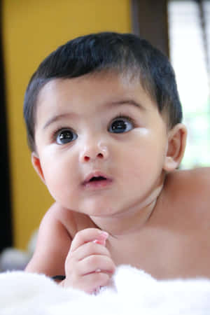 一個深色頭髮、大眼睛的嬰兒，正躺在白色蓬鬆的毯子上向上看。