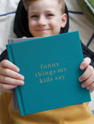 一個快樂的孩子拿著一本青綠色書，書名為 funny things my kids say。