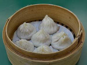 六個蒸餃放在竹蒸籠裡，背景為綠色。