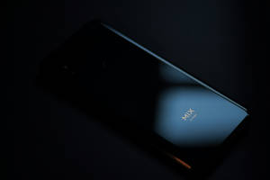 在黑暗環境中，藍光下金色發光的'MIX'標誌的黑色智能手機。 — Xiaomi 壁紙