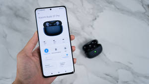 手握住手機顯示耳機設定，實際耳機放在附近的大理石上。 — Xiaomi 壁紙