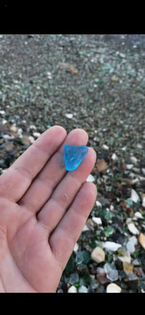 手在散落玻璃的海灘上拿著一塊藍色海玻璃。 — Xiaomi 壁紙