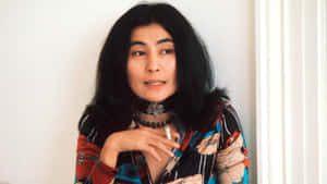 一位長黑髮的女性在室內手持香煙，對著鏡頭微笑。