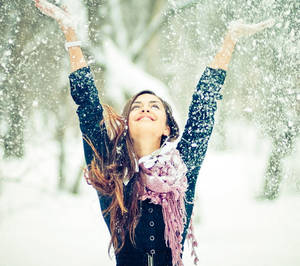 女性在冬季森林中舉起雙臂拋雪。